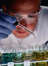 Male researcher wearing eye protection using a dropper to drop liquid into vials